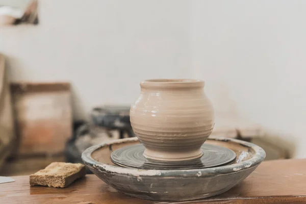 Olla de barro mojado en la rueda de cerámica y esponja en el banco de madera en el estudio de arte - foto de stock