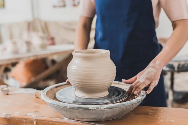 Partial view of young african american woman standing near wet clay pot on wheel in pottery — Stock Photo