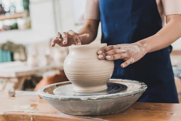 Partial view of young african american woman modeling wet clay pot on wheel in pottery — Stock Photo