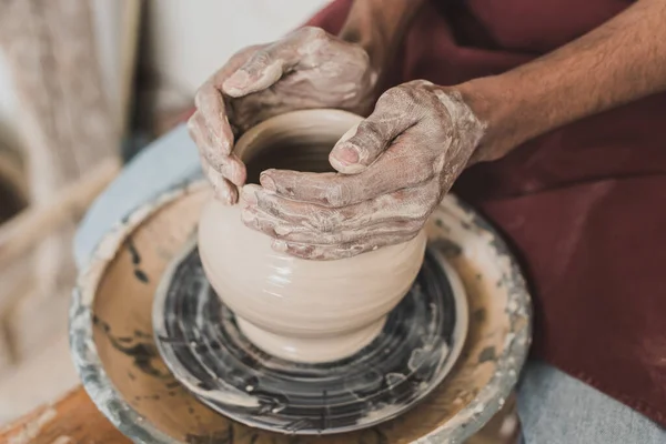 Close up view of young african american man modeling wet clay pot on wheel with hands in pottery — Stock Photo