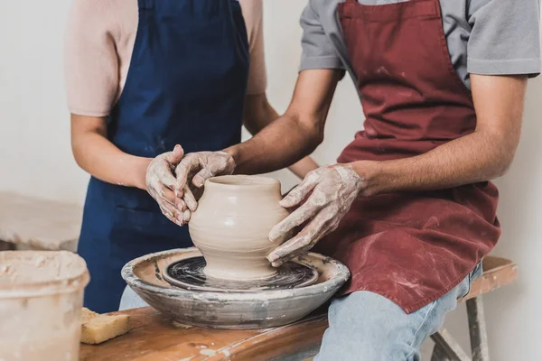 Vista parziale della giovane coppia afro-americana che modella pentola di argilla bagnata su ruota con le mani in ceramica — Foto stock