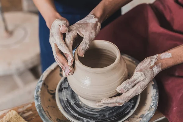 Vue partielle du jeune couple afro-américain modeler pot d'argile humide sur roue avec les mains en poterie — Photo de stock