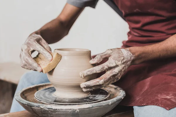 Partial view of young african american man modeling wet clay pot on wheel with hands in pottery — Stock Photo