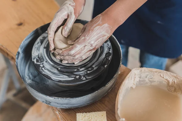 Vista parziale di giovane donna afro-americana modellare pentola di argilla bagnata sulla ruota vicino spugna e acqua in scatola di plastica in ceramica — Foto stock