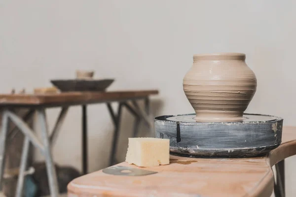 Olla de barro mojado en la rueda de cerámica y esponja en el banco de madera en el estudio de arte - foto de stock