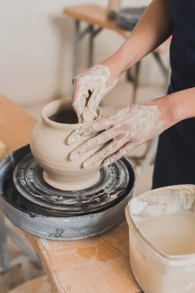 Vista parziale di giovane donna afro-americana modellare pentola di argilla bagnata su ruota con le mani in ceramica — Foto stock