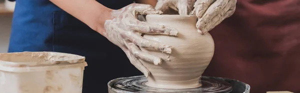 Partial view of young african american couple shaping wet clay pot on wheel with hands in pottery, banner — Stock Photo