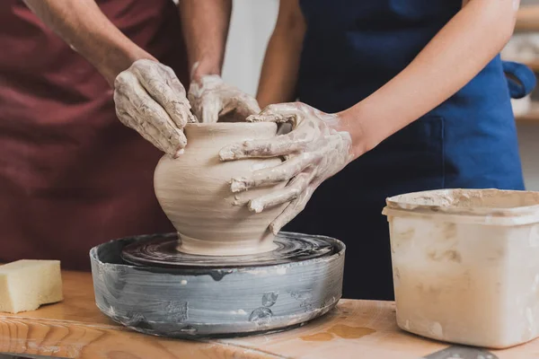 Vue partielle du jeune couple afro-américain façonnant un pot d'argile humide sur roue avec les mains en poterie — Photo de stock