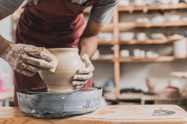 Vue partielle de jeune homme afro-américain faisant pot d'argile humide sur roue avec éponge en poterie — Photo de stock