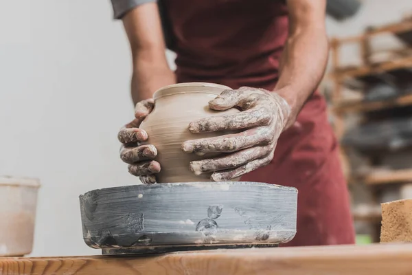 Partial view of young african american man shaping wet clay pot on wheel with hands in pottery — Stock Photo
