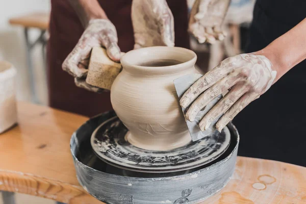 Vue partielle du jeune couple afro-américain façonnant un pot d'argile humide sur roue avec les mains et grattoir en poterie — Photo de stock