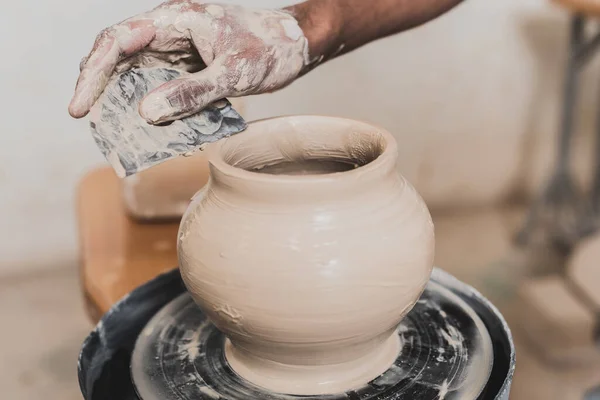 Partial view of male african american hand shaping wet clay pot with scraper in pottery — Stock Photo