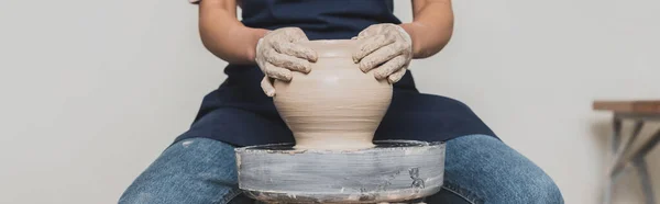 Partial view of young african american woman in apron sitting on bench and shaping wet clay pot in pottery, banner — Stock Photo