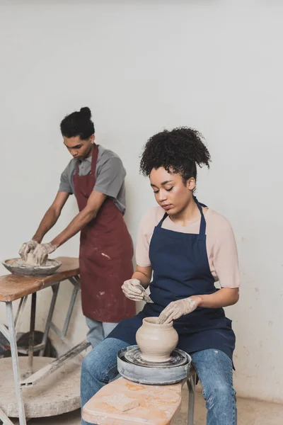 Pareja afroamericana joven concentrada dando forma a ollas de arcilla húmeda en cerámica - foto de stock