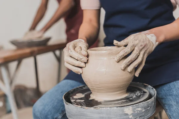 Vista parziale di giovane donna afro-americana modellante pentola di argilla bagnata su ruota con spugna in ceramica — Foto stock