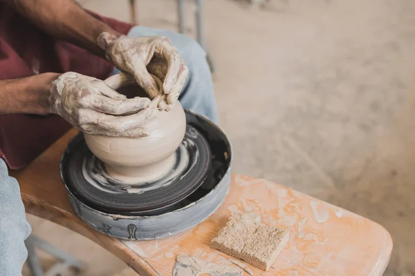 Vista parziale delle mani africane americane maschili che modellano la pentola di argilla bagnata sulla ruota vicino alla spugna e al raschietto in ceramica — Foto stock