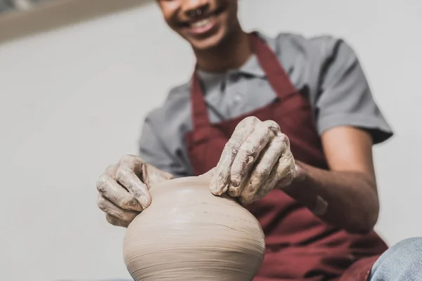 Partial view of young african american man in apron sculpting clay pot in pottery — Stock Photo