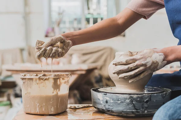 Vue partielle de la jeune femme afro-américaine en tablier sculptant pot sur roue et serrant éponge humide dans la poterie — Photo de stock