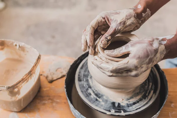 Close up view of male african american hands sculpting clay pot on wheel in pottery — Stock Photo