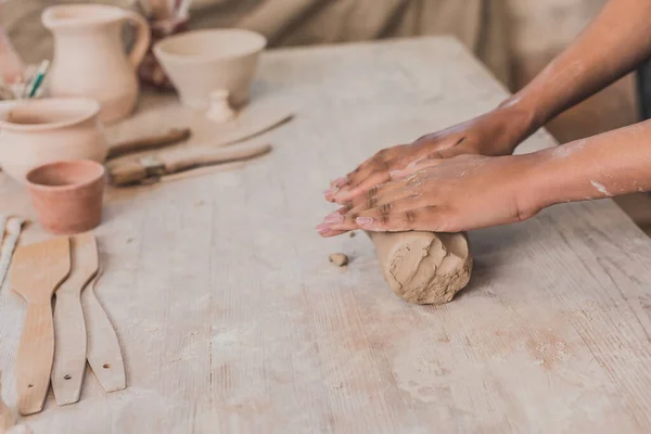 Vue partielle des mains féminines afro-américaines déroulant un morceau d'argile sur une table en bois en poterie — Photo de stock