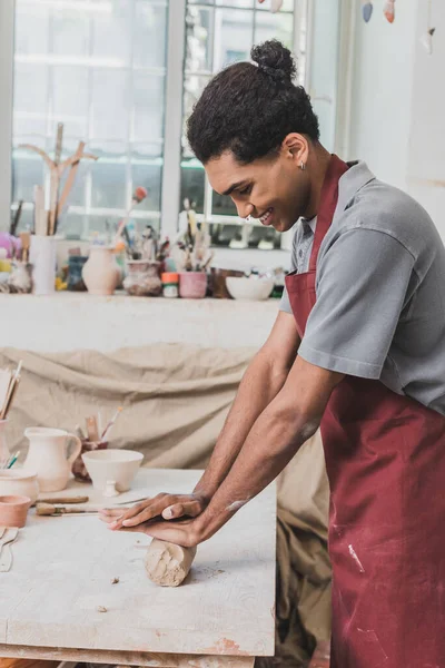 Sonriente joven afroamericano en delantal trabajando con arcilla en cerámica - foto de stock