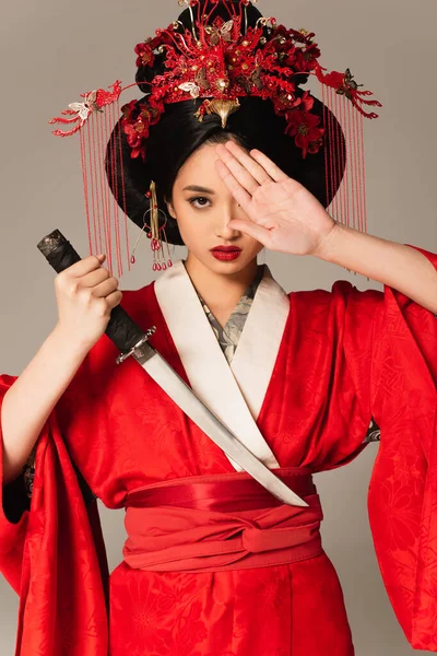 Mujer japonesa sosteniendo espada y cubriendo ojo aislado en gris - foto de stock