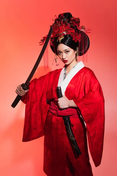 Jeune femme asiatique en kimono tenant épée et gaine sur fond rouge — Photo de stock