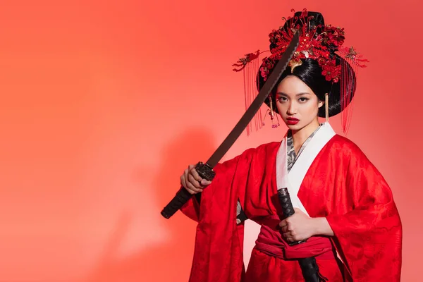 Femme asiatique avec épée regardant la caméra sur fond rouge — Photo de stock