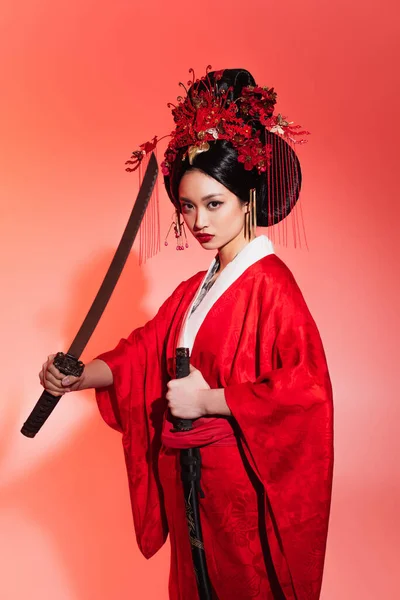 Mujer japonesa en traje auténtico sosteniendo vaina y espada sobre fondo rojo - foto de stock