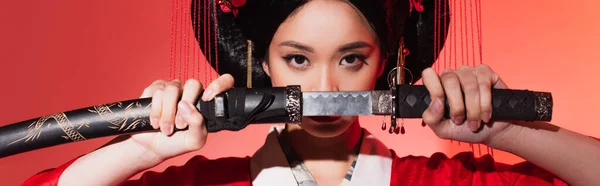 Japanese woman covering face with sword on red background, banner — Stock Photo
