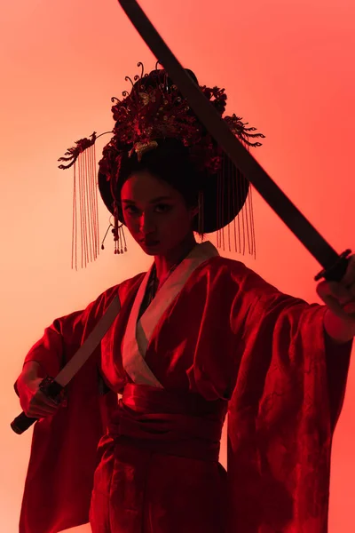 Mujer asiática con espadas mirando a la cámara sobre fondo rojo - foto de stock