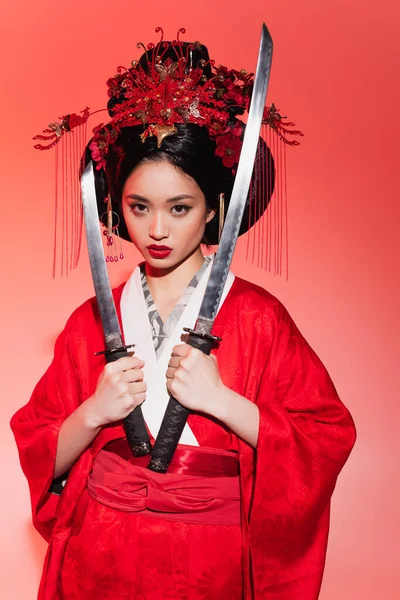 Japanese woman in traditional costume holding swords on red background — Stock Photo