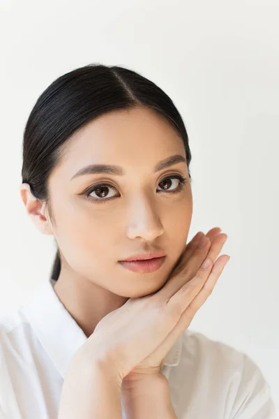 Asian woman in white shirt holding hands near face isolated on grey — Stock Photo