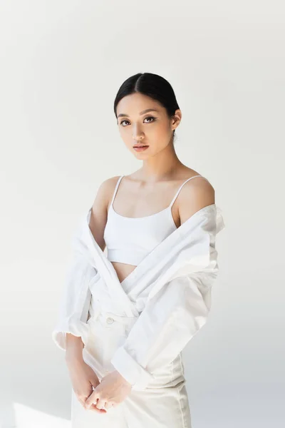 Pretty asian woman in white top looking at camera on grey background — Stock Photo