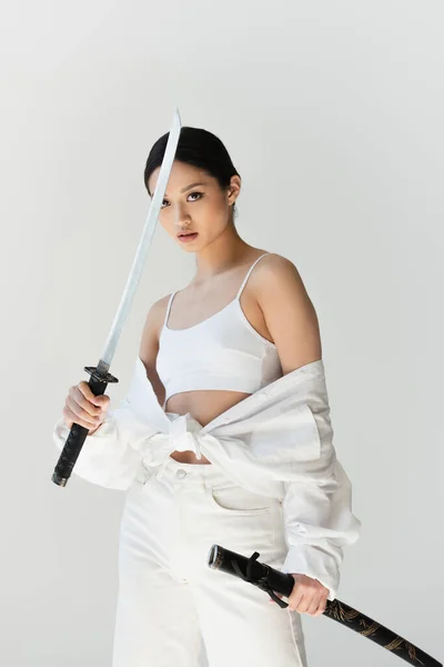 Schöne asiatische Frau in weißen Kleidern mit Schwert isoliert auf grau — Stockfoto