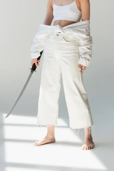 Cropped view of woman in white clothes holding sword on grey background — Stock Photo