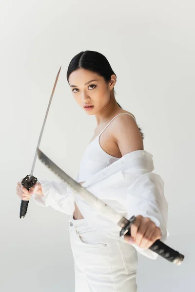 Красива японка з розмитими мечами стоїть ізольована на сірих. — стокове фото