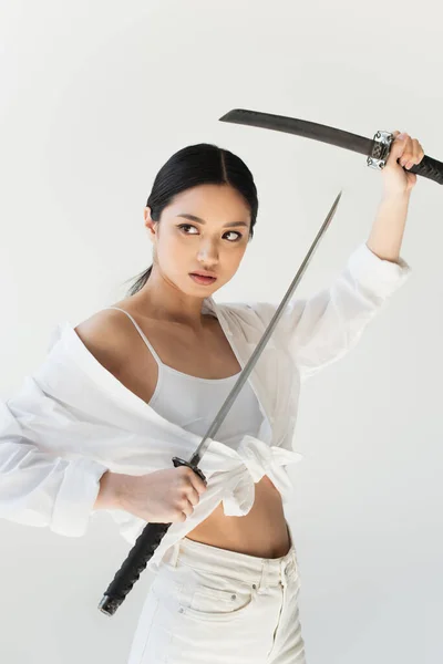 Mujer asiática con arma mirando hacia otro lado aislada en gris - foto de stock