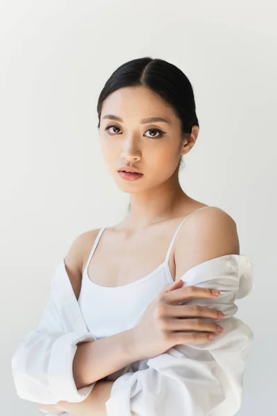 Young asian woman in white clothes touching arm isolated on grey — Stock Photo