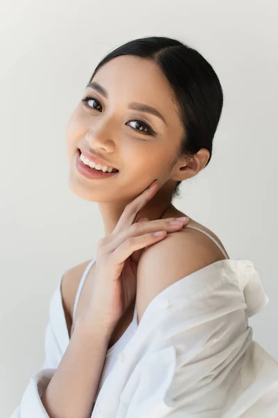 Mujer japonesa con el dedo cerca de la mejilla sonriendo aislada en gris - foto de stock