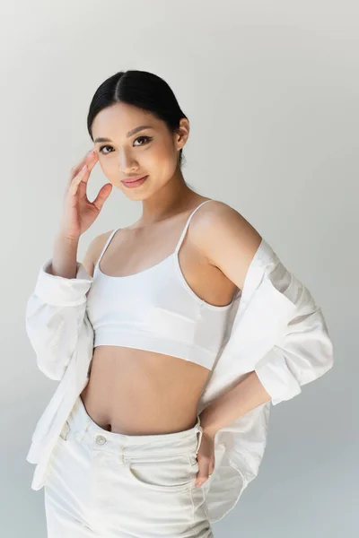 Pretty asian woman smiling at camera while posing isolated on grey — Stock Photo