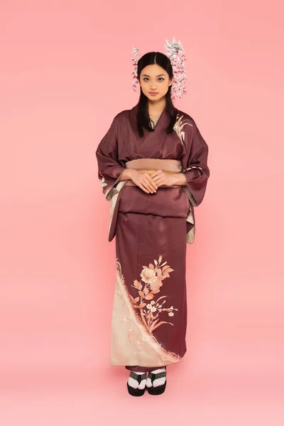 Lunghezza completa della donna asiatica in kimono e infradito guardando la fotocamera su sfondo rosa — Foto stock