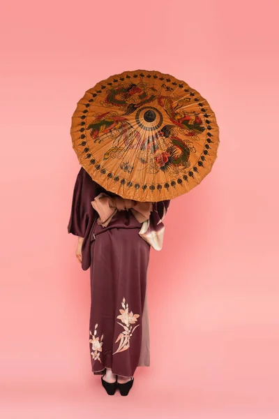 Back view of asian woman holding traditional umbrella on pink background — Stock Photo