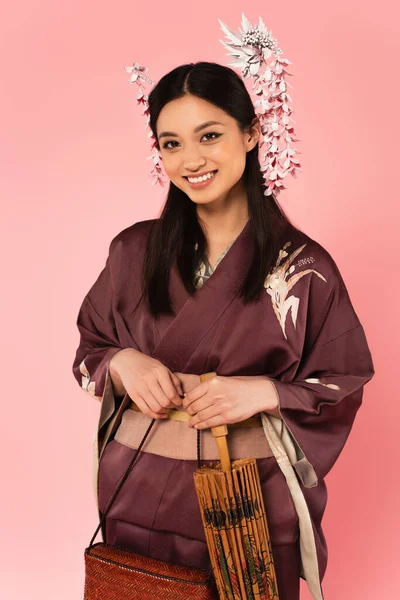 Sorridente donna giapponese in possesso di borsa e ombrello isolato su rosa — Foto stock