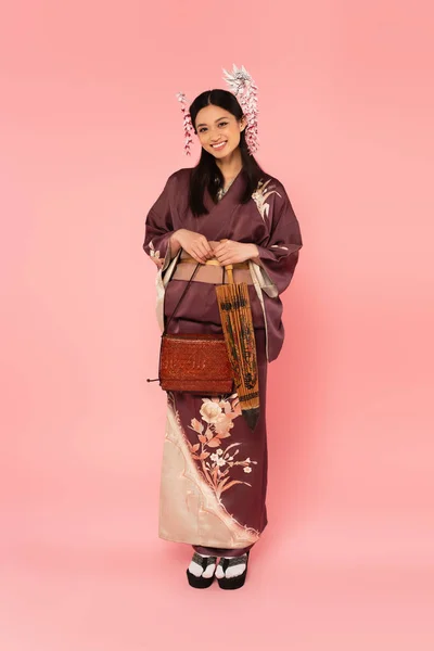 Japanese woman in kimono holding umbrella and handbag on pink background — Stock Photo