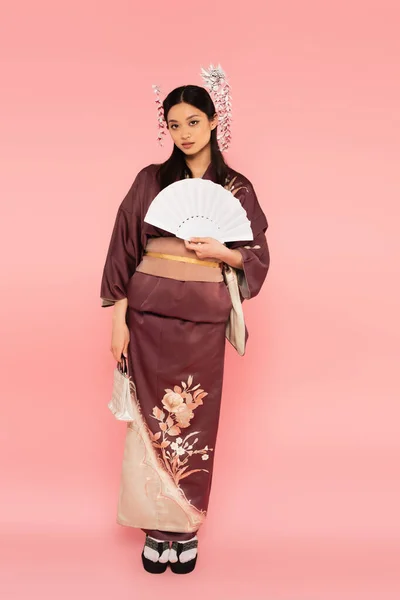 Comprimento total de mulher asiática com bolsa e ventilador de pé sobre fundo rosa — Fotografia de Stock
