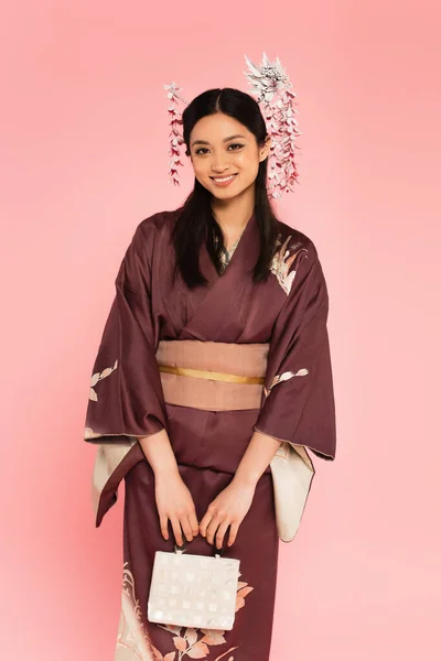 Positivo asiatico donna in kimono holding borsa isolato su rosa — Foto stock