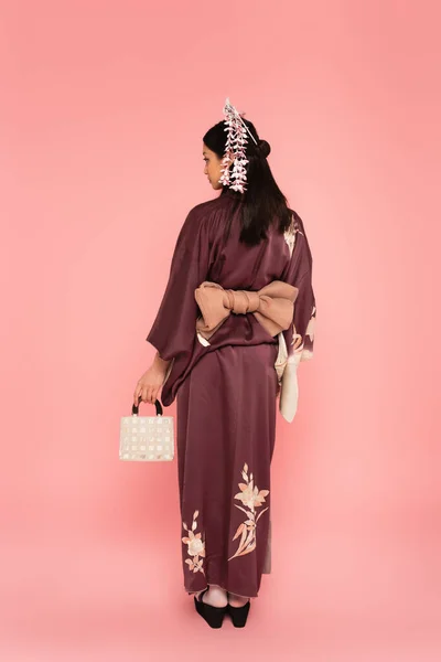 Side view of asian woman in kimono holding handbag on pink background — Stock Photo