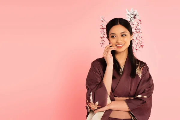 Sonriente asiático mujer en oriental ropa mirando lejos aislado en rosa - foto de stock