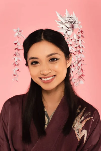 Fröhliche asiatische Frau in traditioneller Kleidung und Frisur schaut in die Kamera isoliert auf rosa — Stockfoto